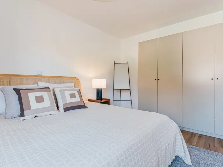 Master bedroom of the Stay Eden MOONSTONE GREEN apartment in Ramstein, featuring a large bed, soft neutral tones, and a spacious wardrobe.
