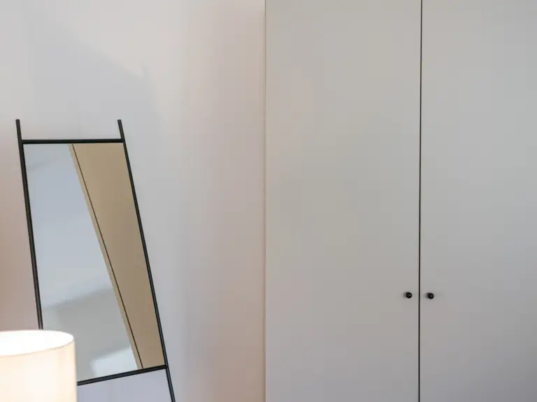 Master bedroom in the Stay Eden MOONSTONE GREEN apartment in Ramstein, featuring a spacious wardrobe and a large mirror with modern décor.