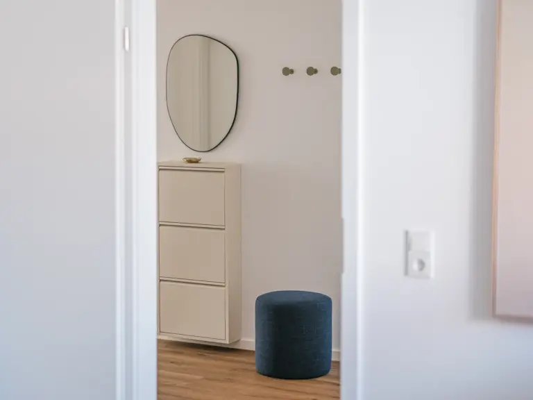 Entrance wardrobe with mirror, shoe cabinet, coat hooks and seating stool at Stay Eden MOONSTONE GREEN Ramstein TLA apartment.