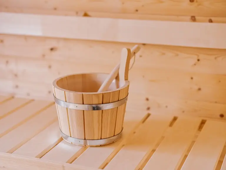 Wooden bucket and ladle inside the Finnish sauna at the Stay Eden SAPPHIRE BLUE apartment in Ramstein, placed on traditional sauna benches.